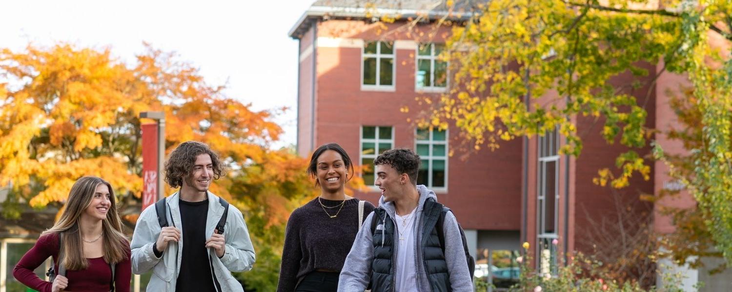 四名SPU学生, three male students and a female student, walking on campus with the Eaton Science Building in the background.